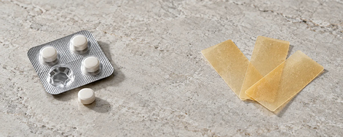 Sublingual tablets in a blister pack next to three thin oral dissolvable strips on a pale stone surface