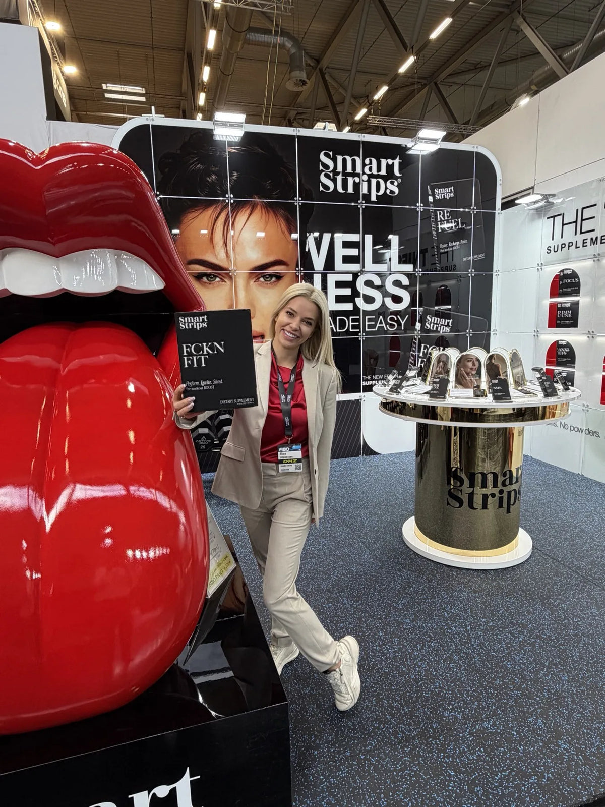 The Smart Strips booth at FIBO 2026 in Cologne, with the giant red lips sculpture and the Wellness Made Easy wall