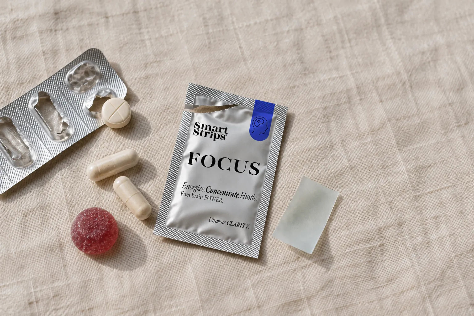 Tablets in a blister, two capsules, a gummy and an open Smart Strips FOCUS sachet with the strip, on linen