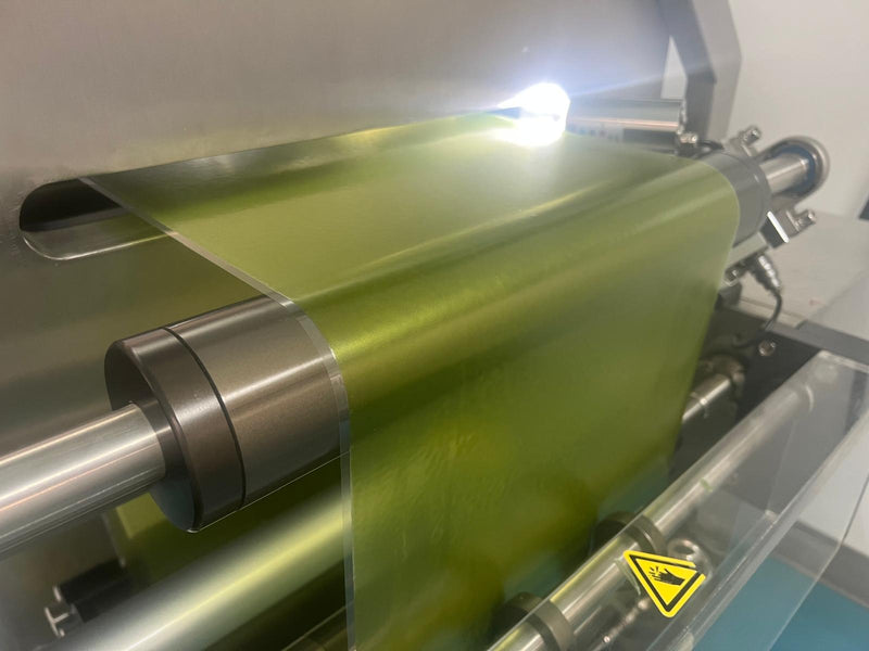 Roll of green material on a machine with a warning label.